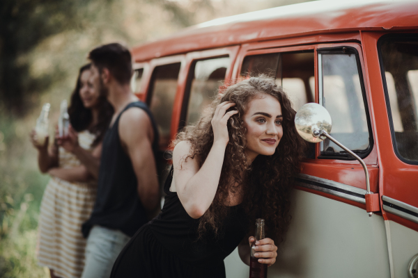 A group of young friends with drinks standing outdoors on a roadtrip through countryside, holding bottles.