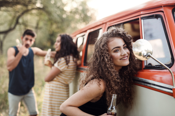 A group of young friends with drinks standing outdoors on a roadtrip through countryside, holding bottles.