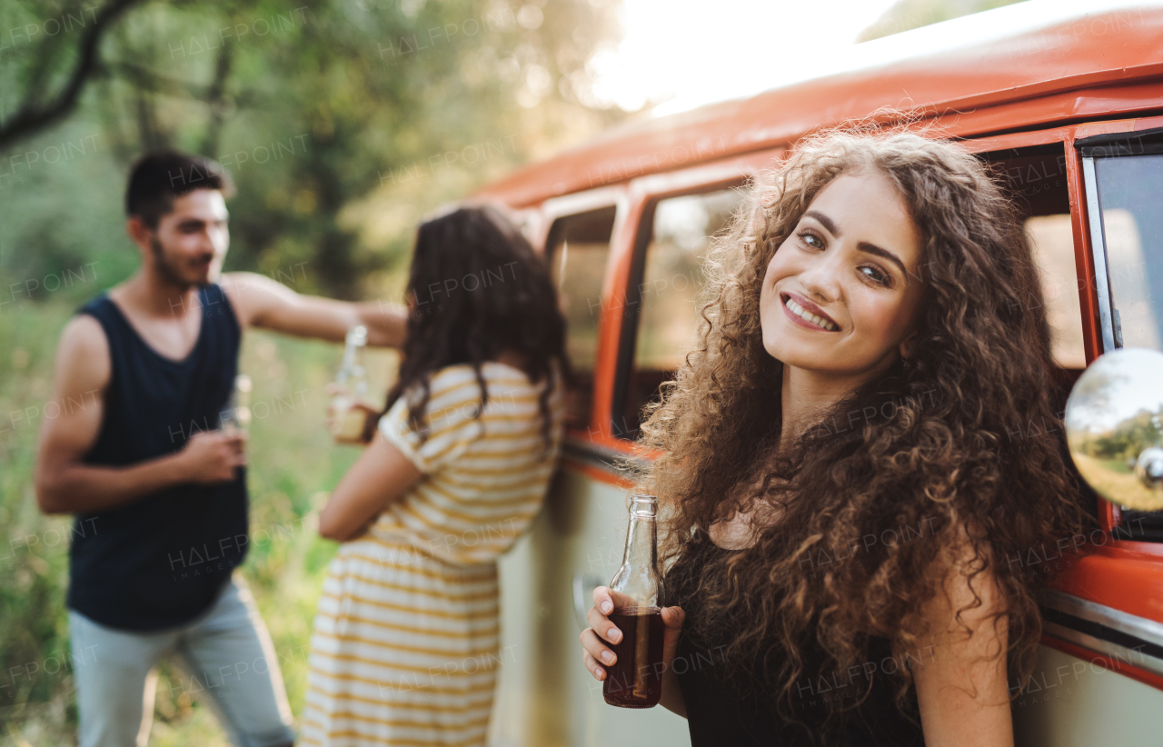 A group of young friends with drinks standing outdoors on a roadtrip through countryside, holding bottles.