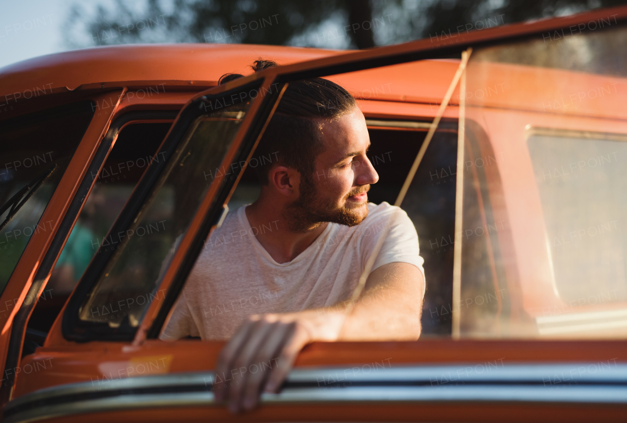 A cheerful young man getting out of a car on a roadtrip through countryside.