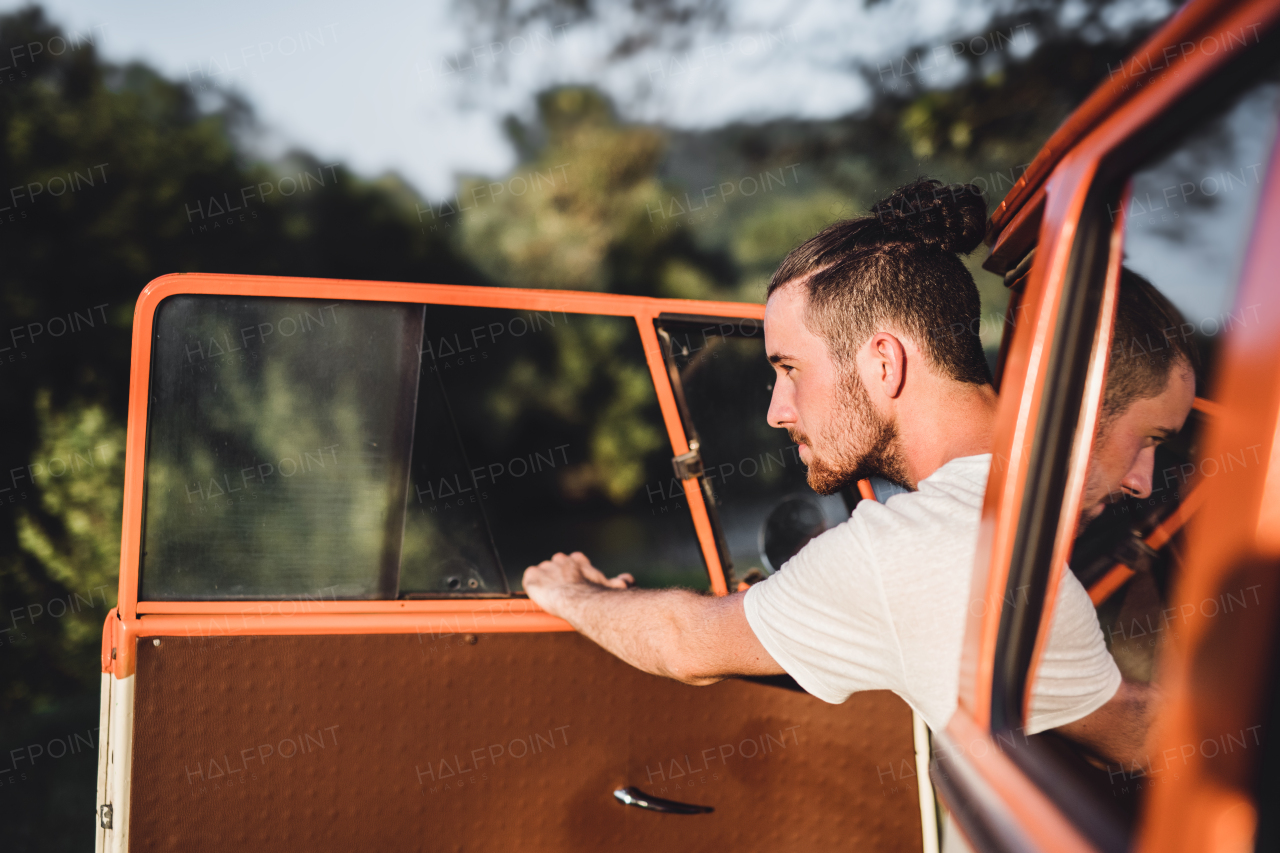 A cheerful young man getting out of a car on a roadtrip through countryside.