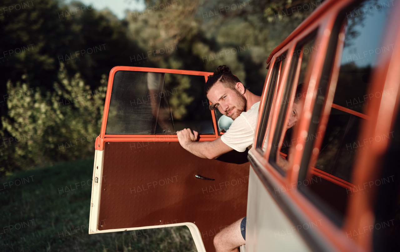 A cheerful young man getting out of a car on a roadtrip through countryside. Copy space.