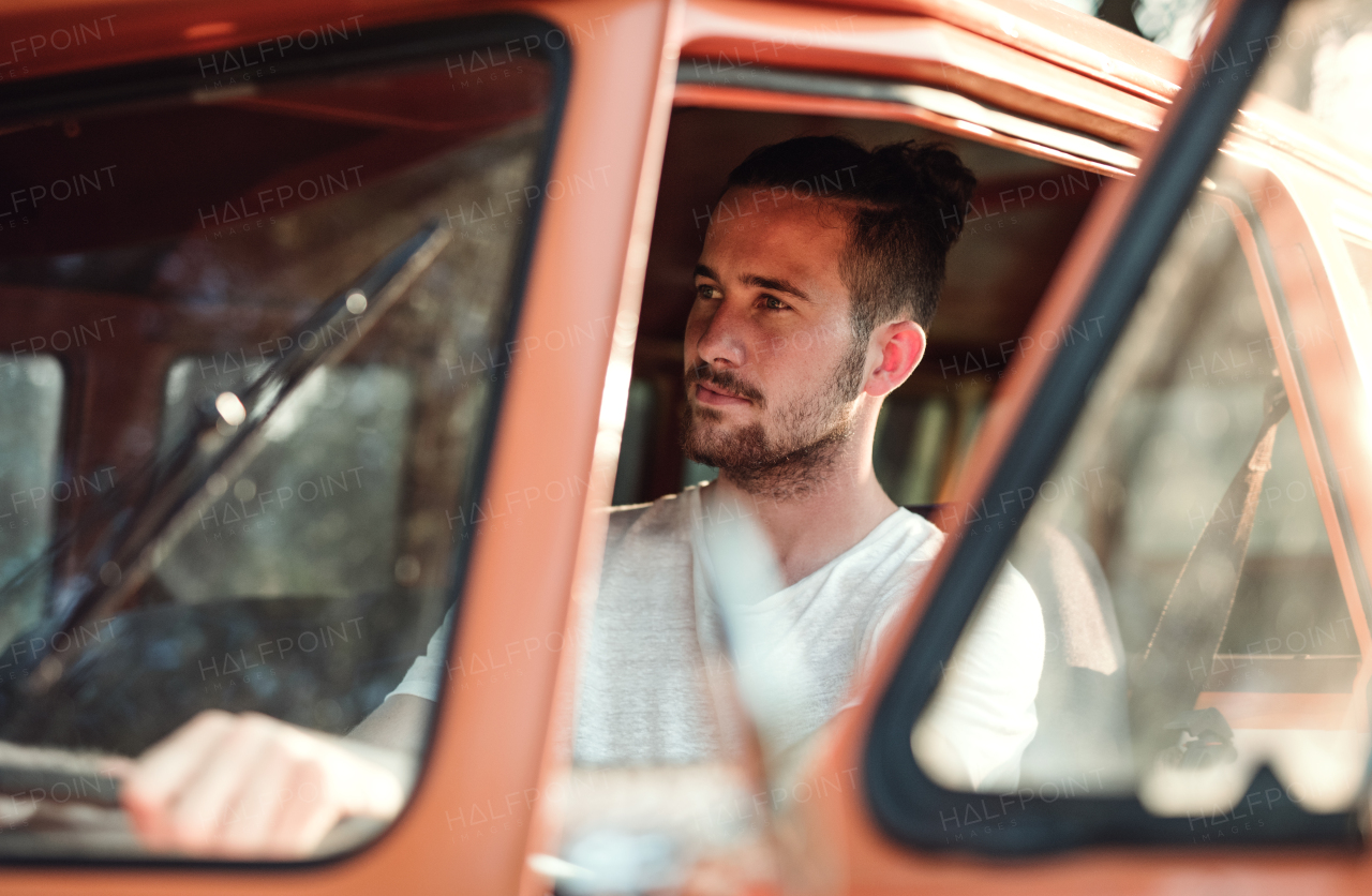 A cheerful young man driving a car on a roadtrip through countryside.