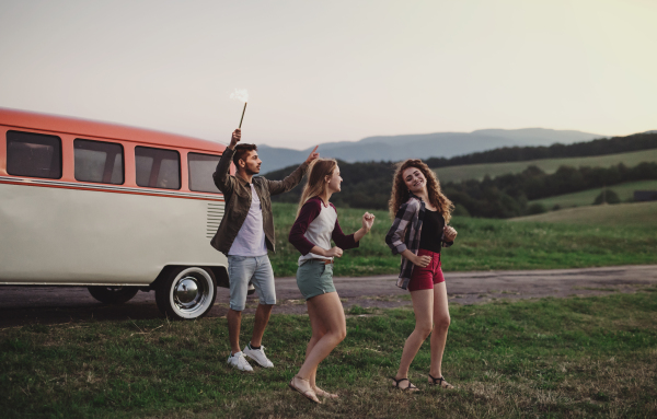 A group of young friends with drinks standing outdoors on a roadtrip through countryside, dancing.