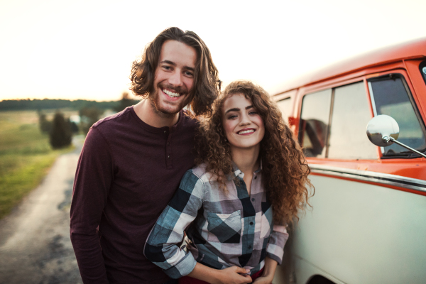 A young couple on a roadtrip through countryside, standing by retro minivan.