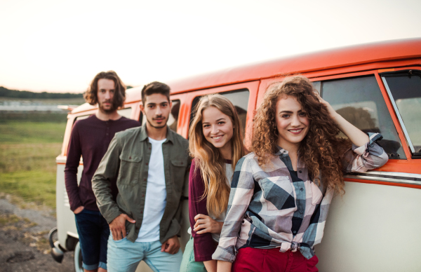 A group of young friends on a roadtrip through countryside, standing by a retro minivan.