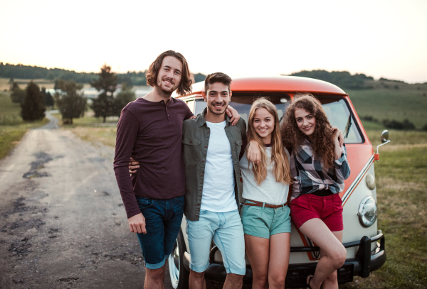 A group of young friends on a roadtrip through countryside, standing by a retro minivan.