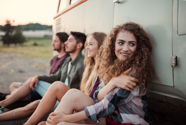 A group of young friends on a roadtrip through countryside, sitting by a retro minivan.