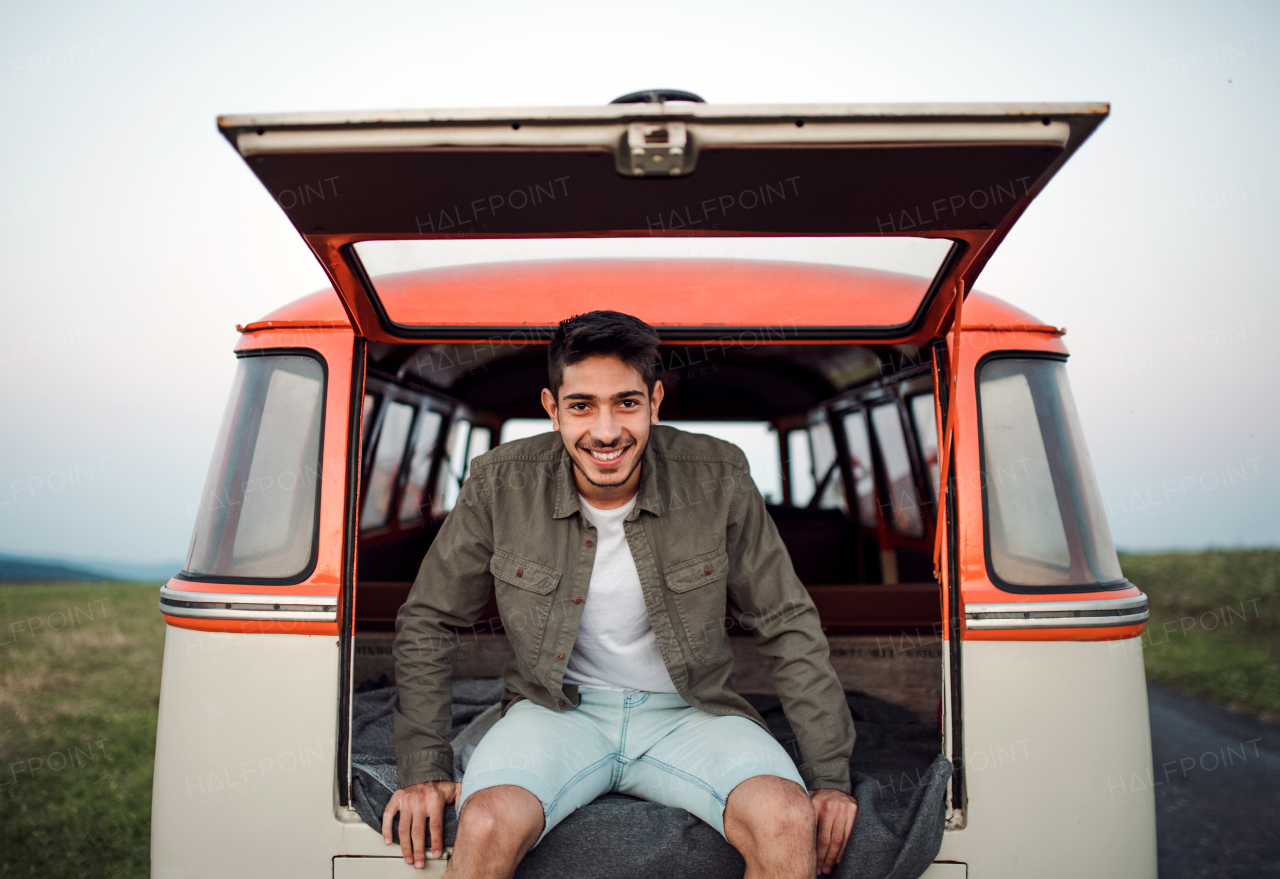 A young hispanic man sitting in a car on roadtrip through countryside. Front view.