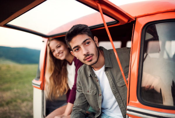 A young couple on a roadtrip through countryside, sitting in retro minivan.