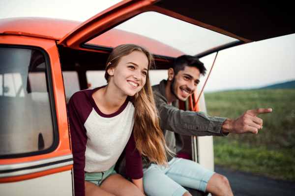 A young couple on a roadtrip through countryside, sitting in retro minivan.