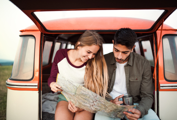 A young couple on a roadtrip through countryside, sitting in retro minivan and looking at a map.