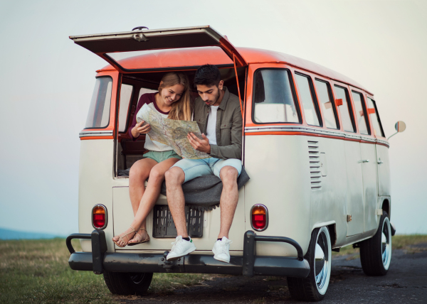 A young couple on a roadtrip through countryside, sitting in retro minivan and looking at a map.