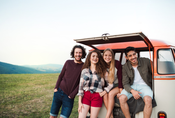 A group of young friends on a roadtrip through countryside, standing by a retro minivan.