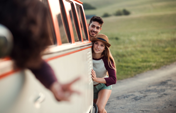 A group of young friends pushing a retro minivan on a roadtrip through countryside.