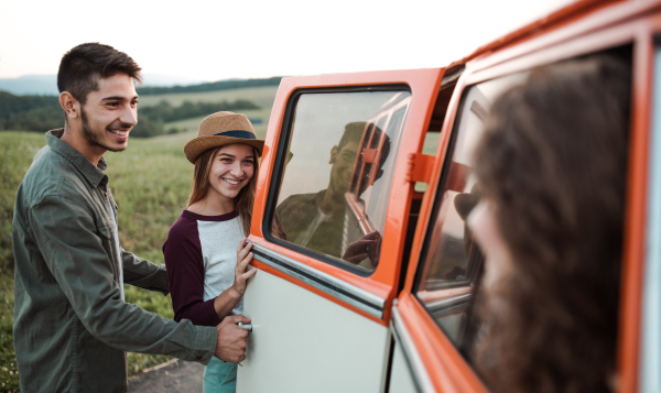 A group of young friends standing by a retro minivan on a roadtrip through countryside.