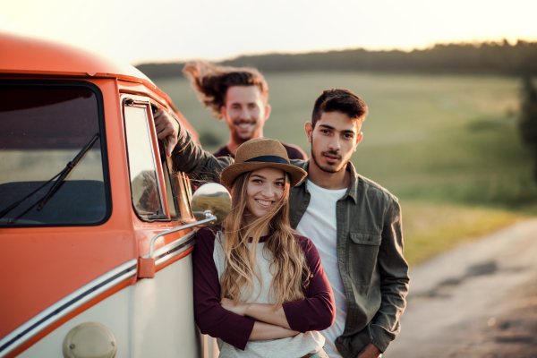 A group of young friends on a roadtrip through countryside, standing by a retro minivan.