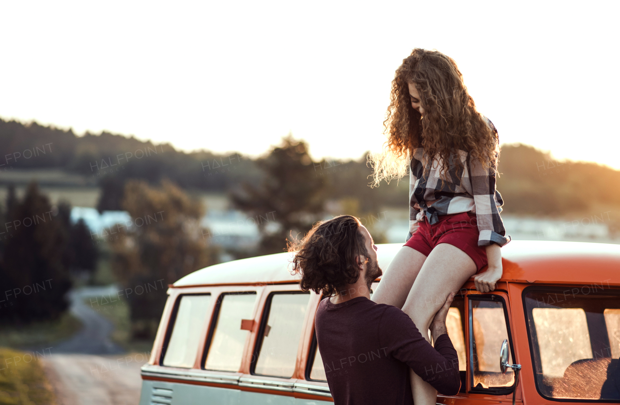 A young couple on a roadtrip through countryside, standing by retro minivan.