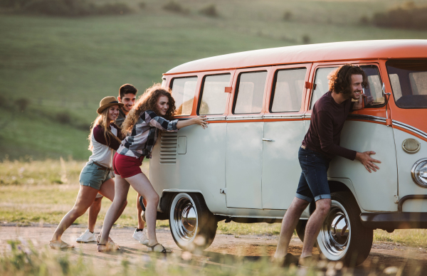 A group of young friends pushing a broken retro minivan car on a roadtrip through countryside.