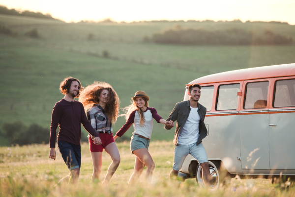 A group of young friends walking in front of a retro minivan on a roadtrip through countryside, running.