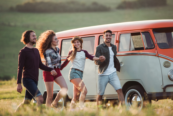 A group of young friends walking by a retro minivan on a roadtrip through countryside, holding hands.