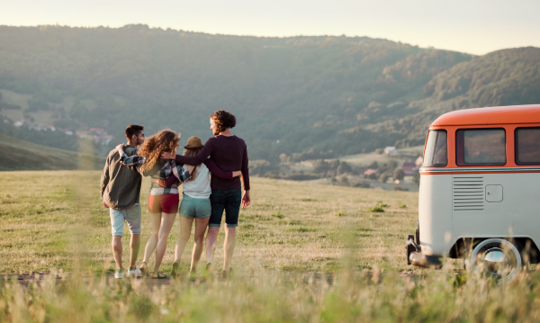 A rear view of group of young friends on a roadtrip through countryside, walking arm in arm.