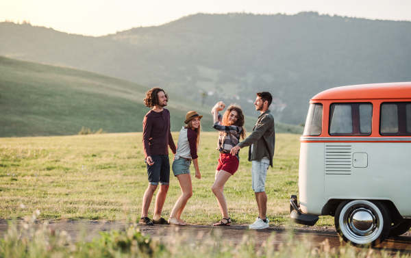 A group of young friends with drinks standing outdoors on a roadtrip through countryside, dancing.