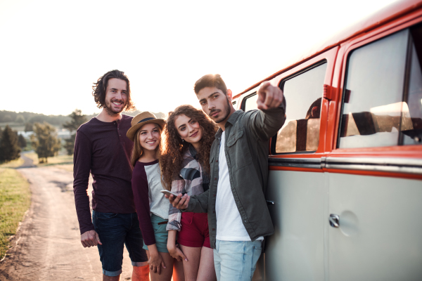 A group of young friends on a roadtrip through countryside, standing by a retro minivan.