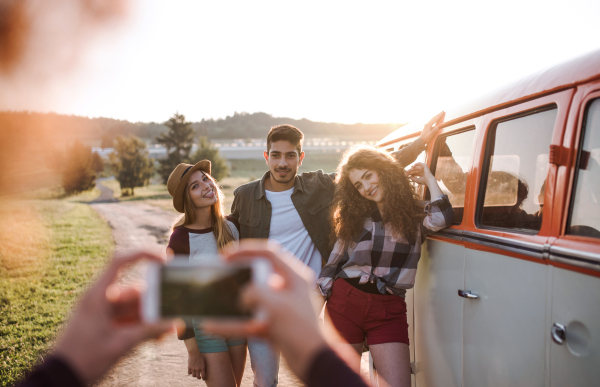 A group of young friends with smartphone on a roadtrip through countryside, taking photograph with smartphone.