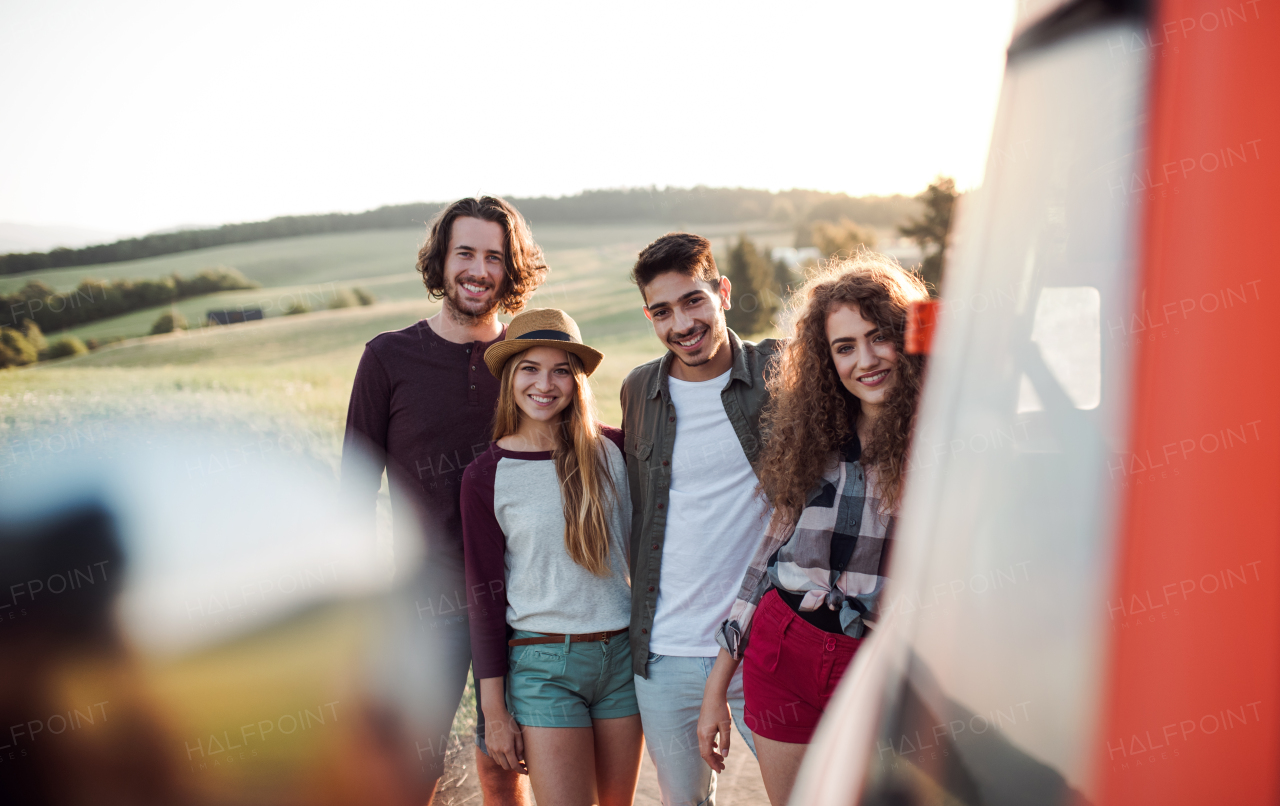 A group of young friends on a roadtrip through countryside, standing by a retro minivan.