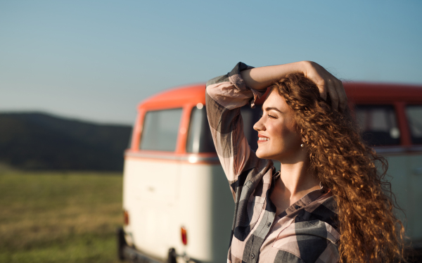 A young girl on a roadtrip through countryside, standing by a minivan. Copy space.