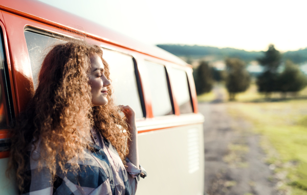 A young girl on a roadtrip through countryside, leaning on a retro minivan, eyes closed. Copy space.