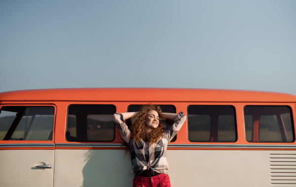 A young girl on a roadtrip through countryside, leaning on a retro minivan, eyes closed. Copy space.