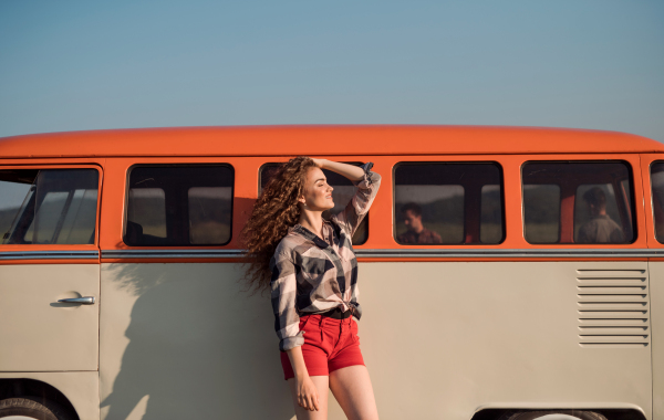 A young girl on a roadtrip through countryside, leaning on a retro minivan, eyes closed. Copy space.