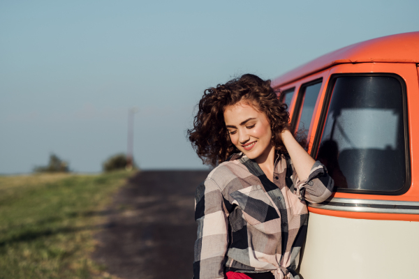 A young girl on a roadtrip through countryside, standing by a minivan. Copy space.