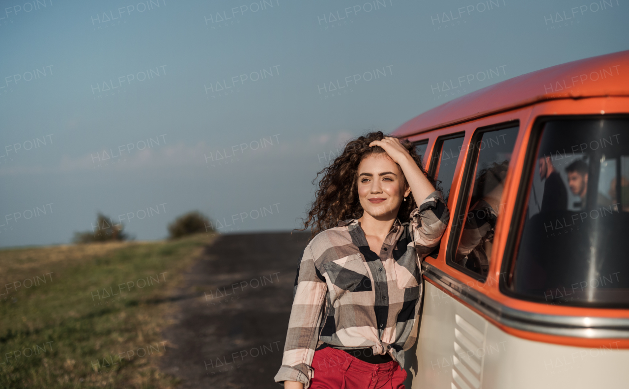 A young girl on a roadtrip through countryside, leaning on a retro minivan. Copy space.