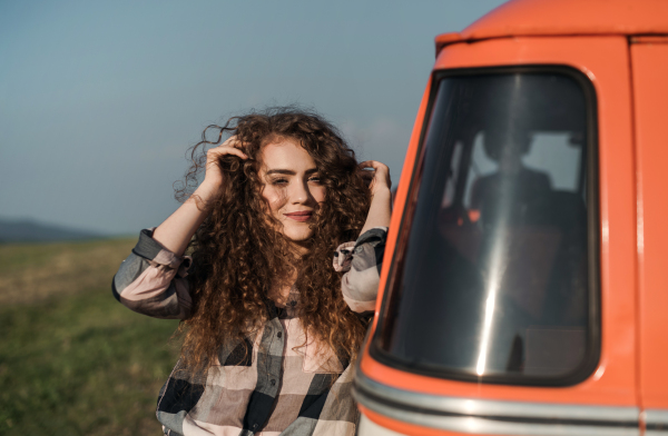 A young girl on a roadtrip through countryside, standing by a minivan. Copy space.