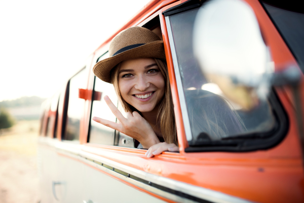 A cheerful young girl looking out of a car on a roadtrip through countryside.