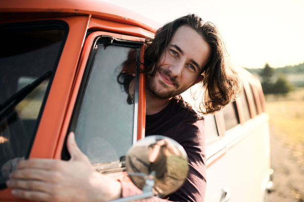 A cheerful young man driving a car on a roadtrip through countryside.