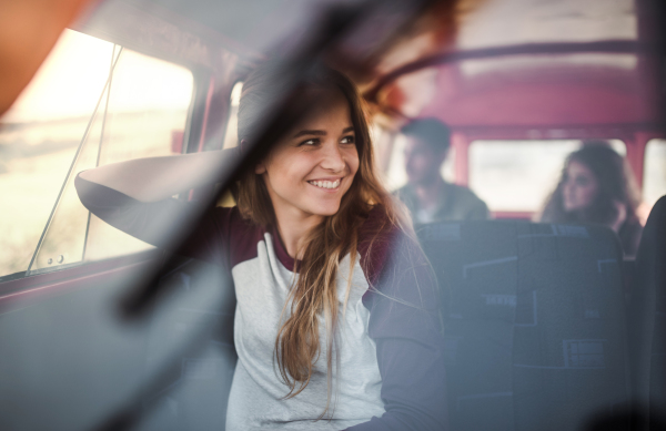 A young cheerful girl in a car on a roadtrip through countryside, shot through glass.