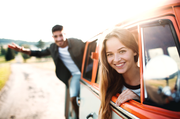 A group of young friends standing by a retro minivan on a roadtrip through countryside.