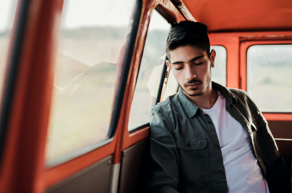 A young tired hispanic man sitting in a car on roadtrip through countryside, sleeping.