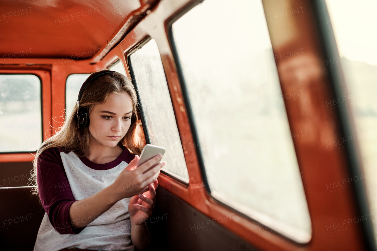 Friends on a roadtrip through countryside, a girl with headphones and smartphone listening to music. Copy space.