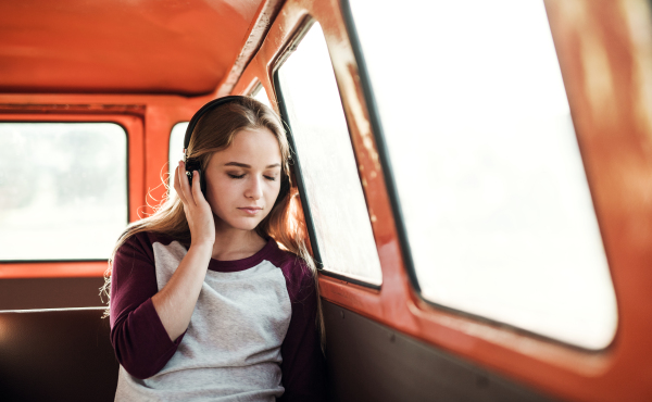 Friends on a roadtrip through countryside, a girl with headphones listening to music. Copy space.