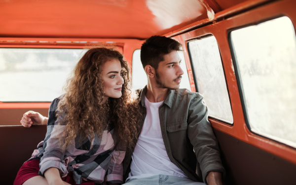 A young couple on a roadtrip through countryside, sitting in retro minivan.