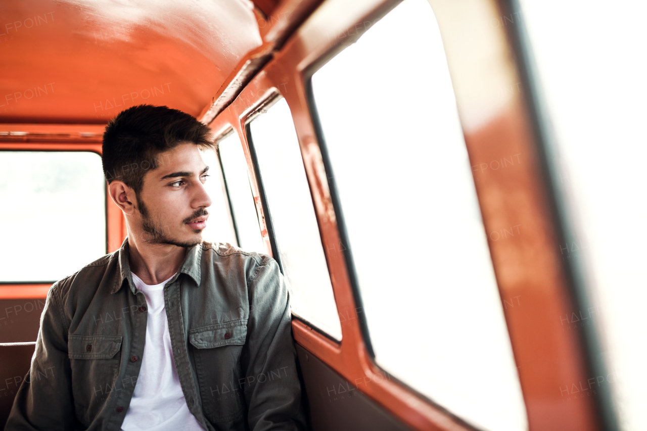 A young hispanic man sitting in a car on roadtrip through countryside. Front view.