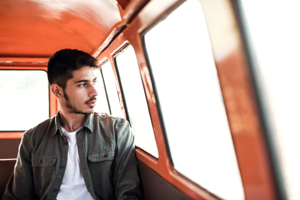 A young hispanic man sitting in a car on roadtrip through countryside. Front view.