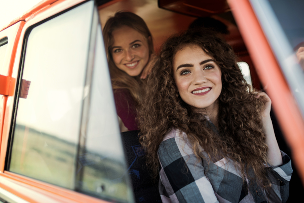 Young female friends on a roadtrip through countryside, looking out of a minivan.