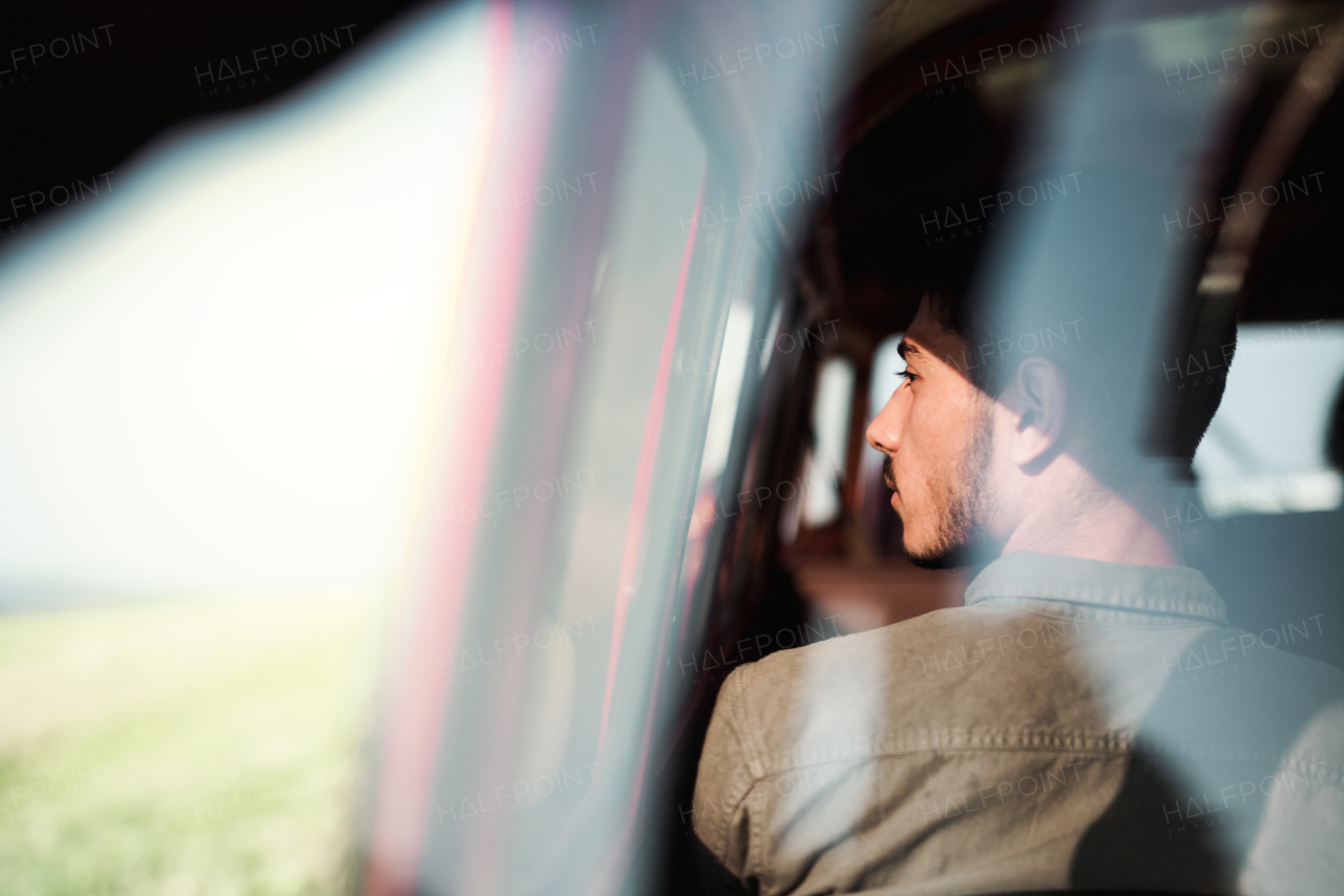 A young hispanic man sitting in a car on roadtrip through countryside, shot through glass. Rear view.