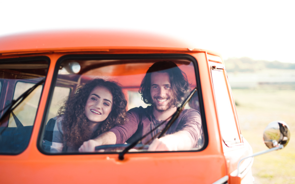 A young couple on a roadtrip through countryside, driving retro minivan.